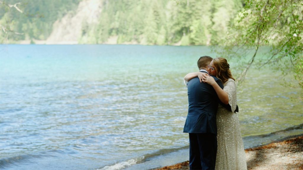 newlywed couple hugging in front of lake in Olympic National Park captured by destination wedding videographer, Alesia Films