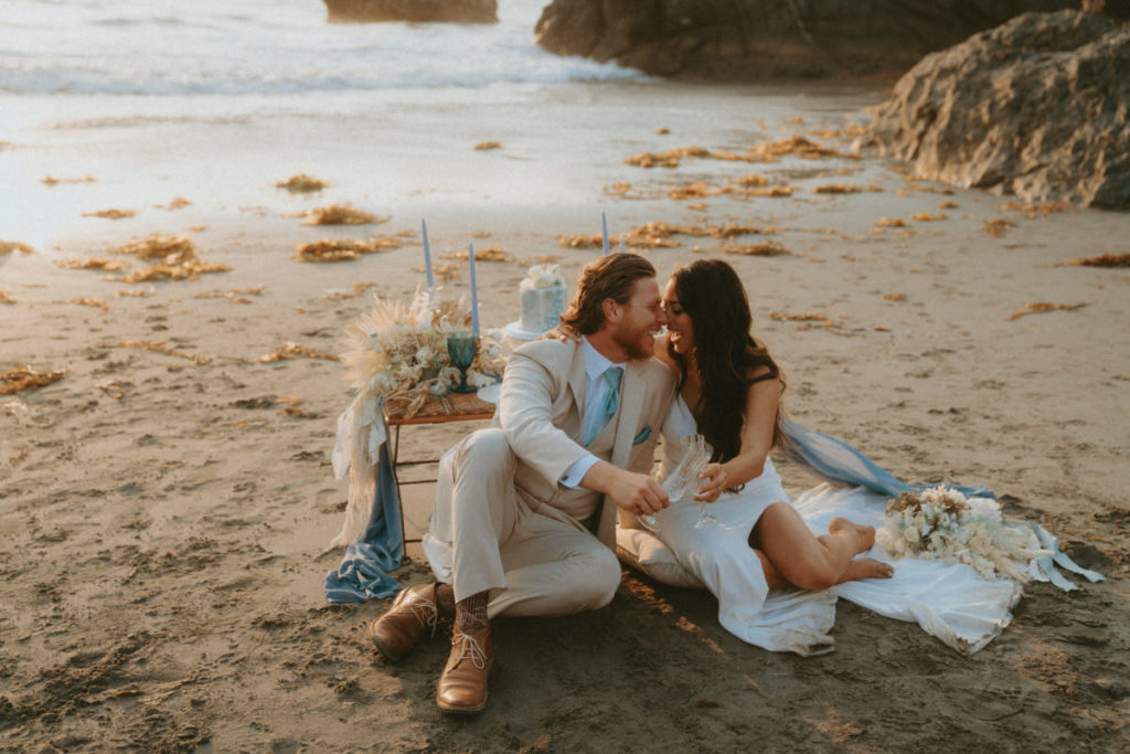 bride and groom sitting down for a beach picnic