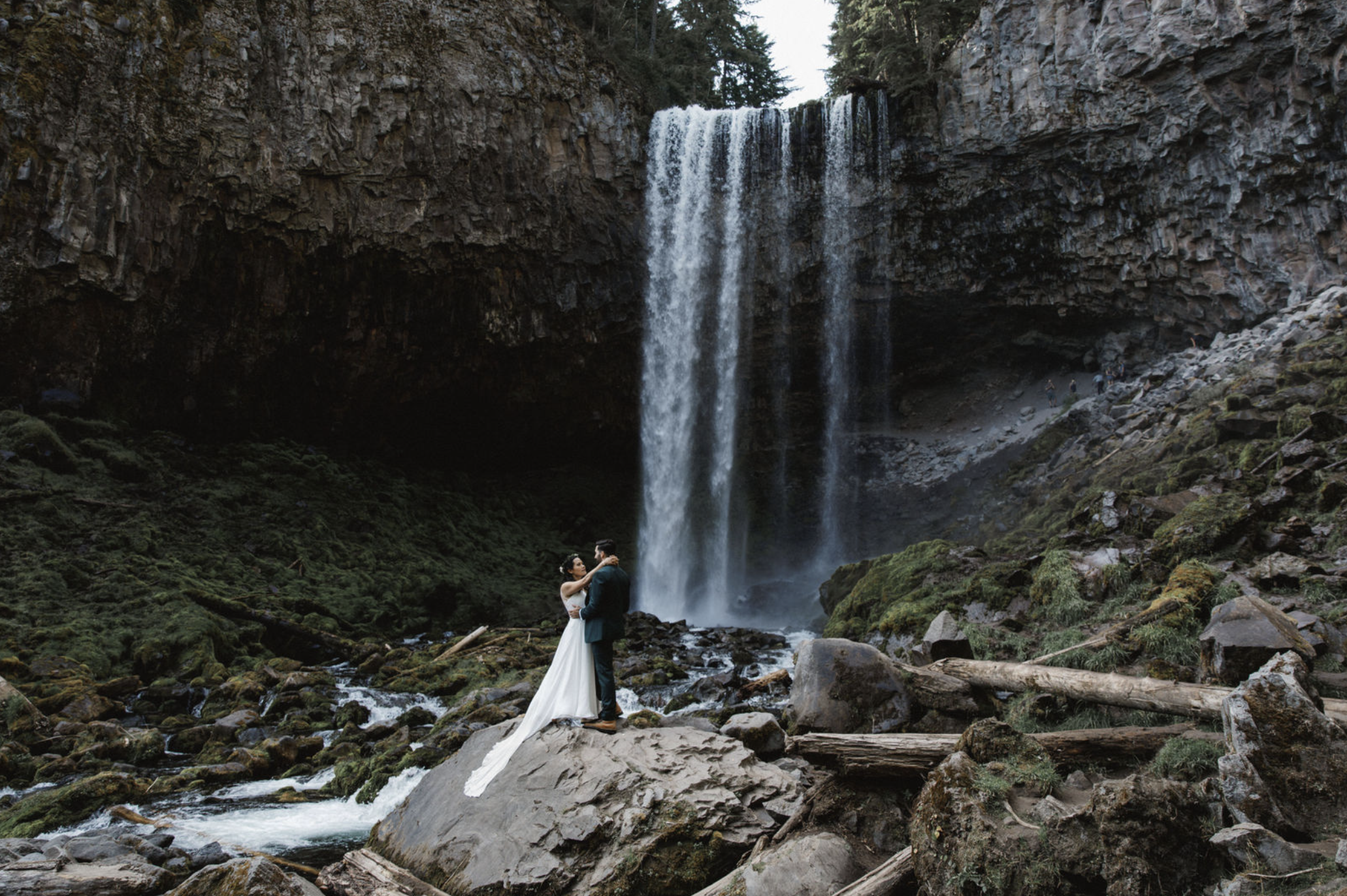 bride and groom standing in front of waterfall