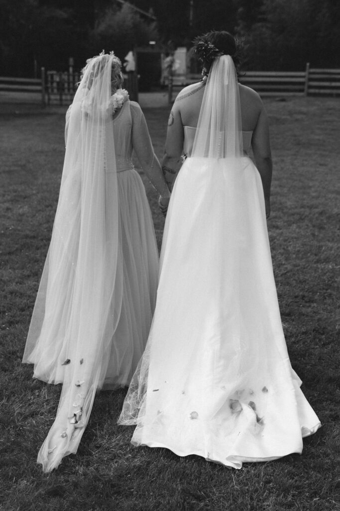 Brides walking away from Orcas Island wedding ceremony with flower petals on gowns