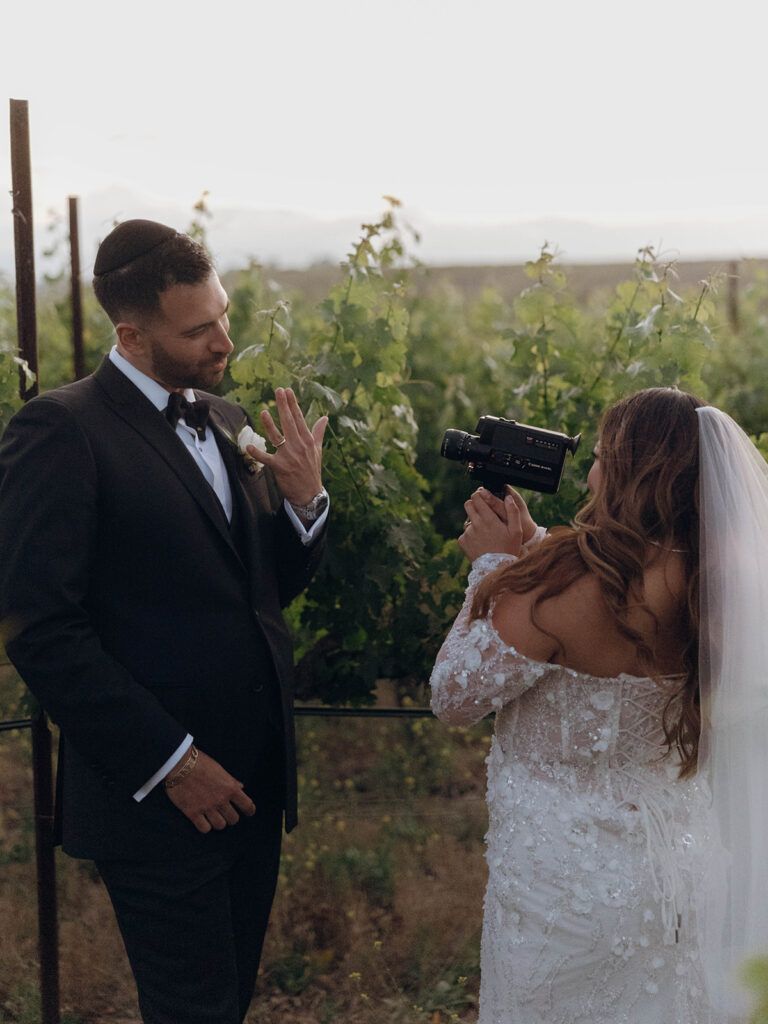 Bride using vintage super 8 camera to film groom during sunset bridal portraits in Temecula