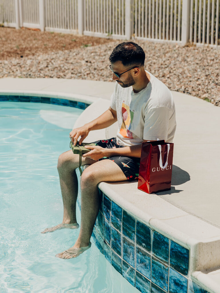 Groom opening wedding day gifts beside swimming pool before Temecula, CA wedding