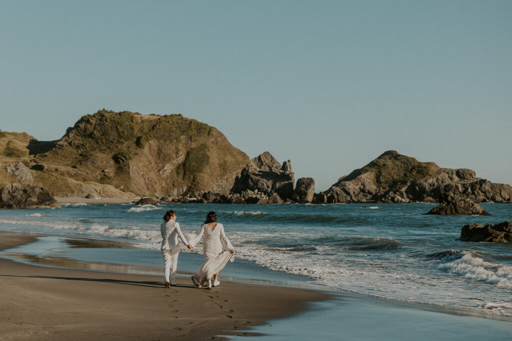 Brides walking hand in hand along coast during redwoods California bridal portraits