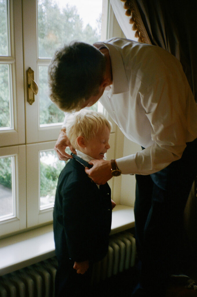 Groom putting a bowtie on his son while getting ready for Italy wedding