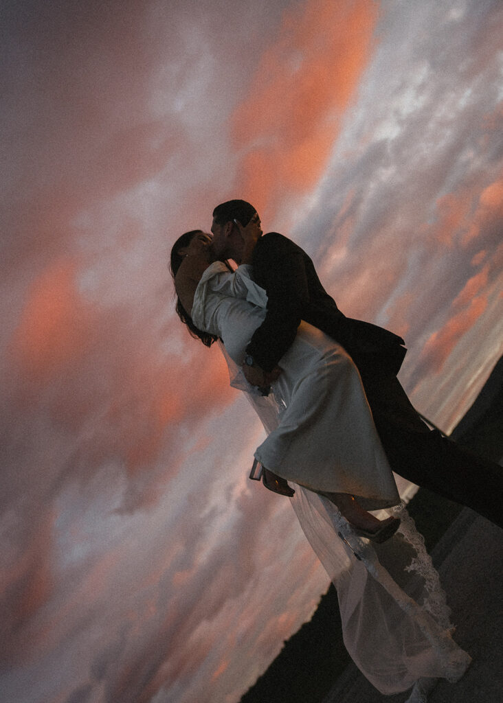 Bride and groom kissing in front of cloudy, sunset skies in Tuscany, Italy