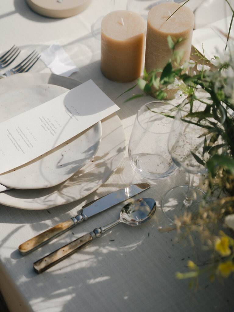 Coastal-inspired wedding tablescape with earthy candles, menus, and ceramic dinnerware