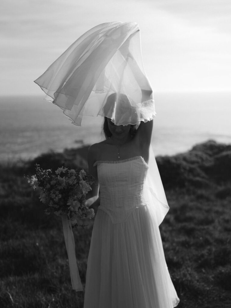 Bride lifting her veil with bouquet in hand during golden hour at Sea Ranch Lodge wedding