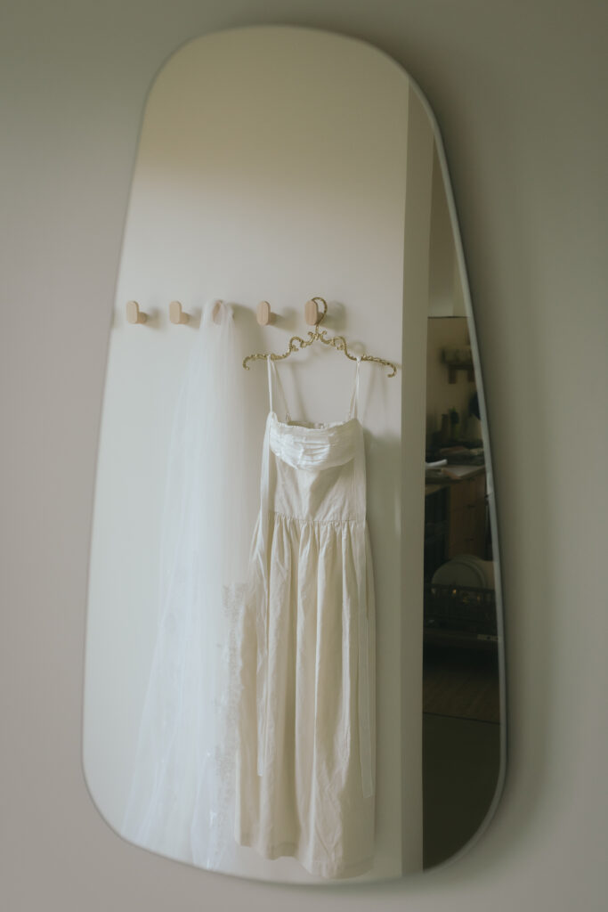 Silk wedding dress and veil hanging on a mirror, ready for the vintage-inspired Oregon Coast elopement.