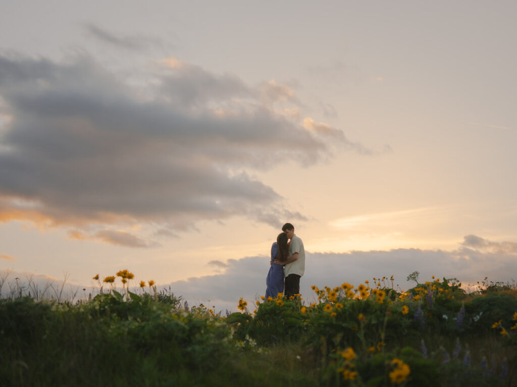 Soft embrace during their Rowena Crest wildflower engagement, surrounded by blooms under a pastel sky.