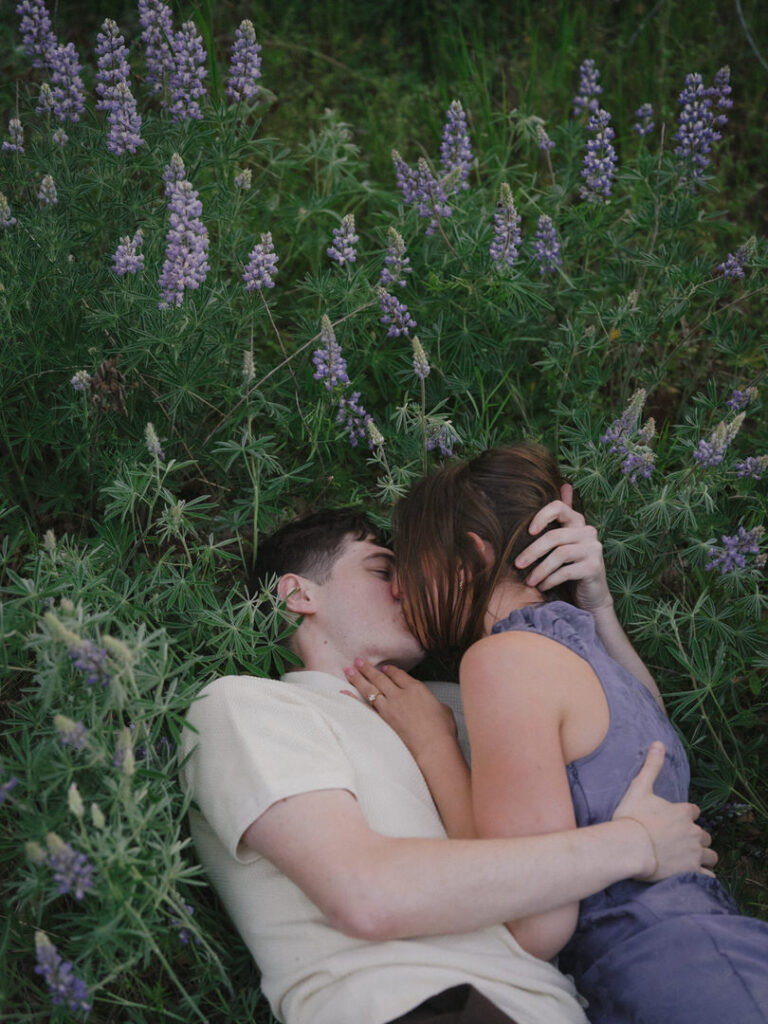 Tender kiss between the couple surrounded by spring lupines.