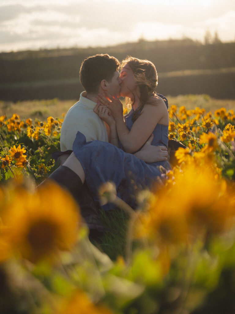 Couple kisses in a golden field of wildflowers at sunset, surrounded by glowing blooms and soft spring light.