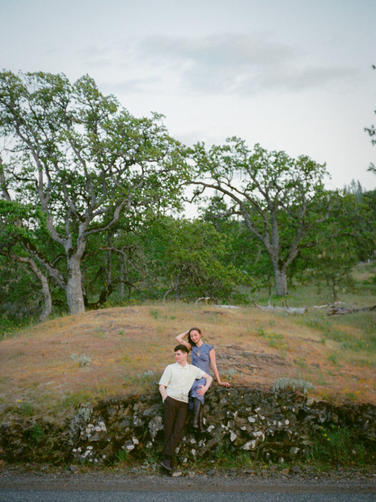 Couple posing on roadside knoll framed by mossy Oregon trees.